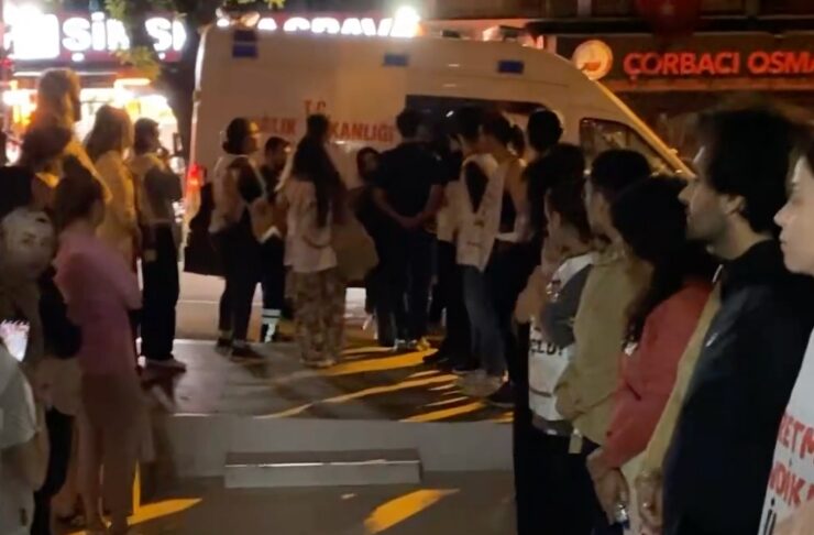 People form two lines along a city street at night, facing a white ambulance parked in the middle.