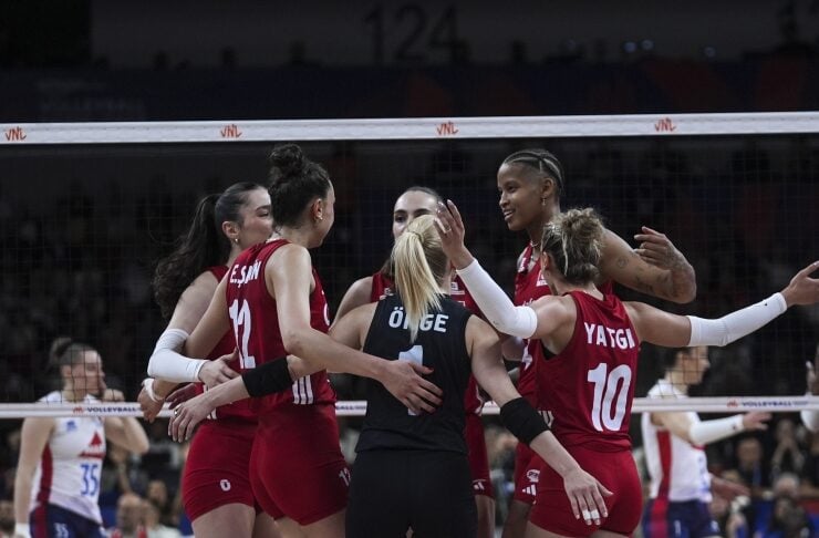 A group of female volleyball players in red uniforms celebrate in a huddle on the court, tying up after a point.