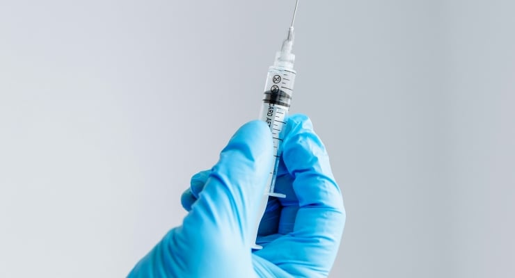 Close-up of a gloved hand drawing liquid into a syringe with a needle attached, medical context shown.