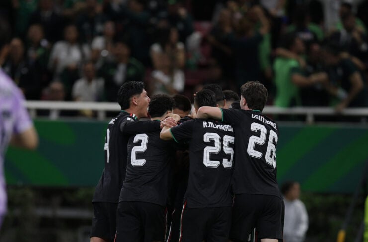 Soccer players in black uniforms celebrate in a tight huddle on the field as teammates embrace after a goal.