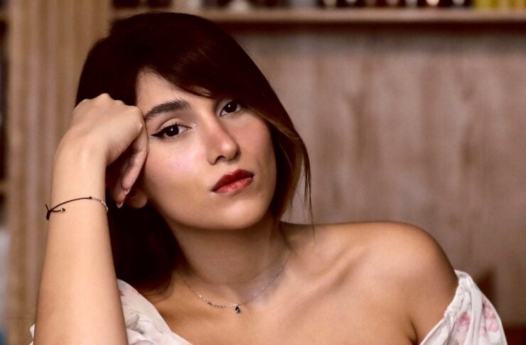 Young woman with dark hair in a floral off‑the‑shoulder top leaning on her elbow, gazing softly at the camera.