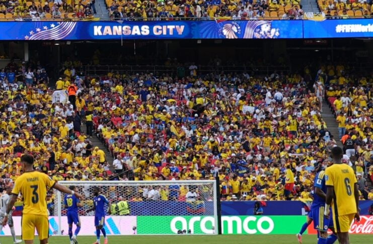Soccer match in a packed stadium with a Kansas City banner; players in yellow on the field near the goal, blue-clad opponents, and a vibrant crowd in yellow in the stands.