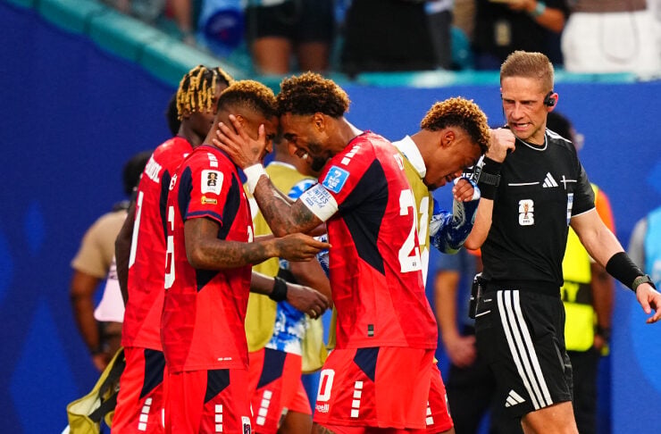 Soccer players in red uniforms celebrate on the field as a referee watches nearby.