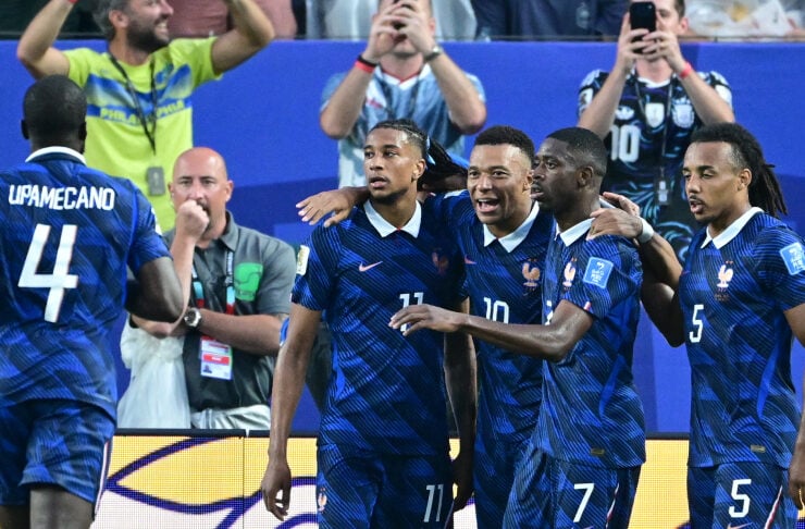 French national team players in blue uniforms celebrate a goal with arms around each other on the field.