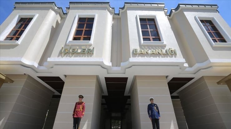 Facade of a government building with gold Turkish signage and two uniformed guards standing at the entrance.