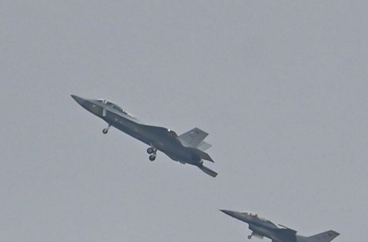 Two fighter jets in a tight formation with landing gear down against a gray sky.