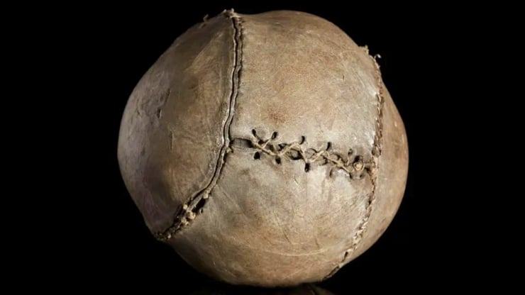 Old, worn baseball with visible stitching on a black background.