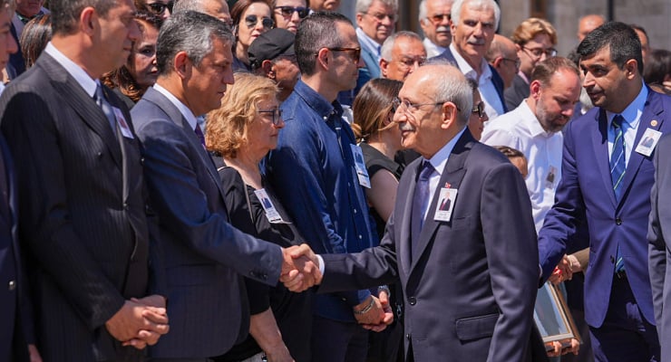 Business leaders in a crowd shake hands at a formal event, name badges visible on attendees.
