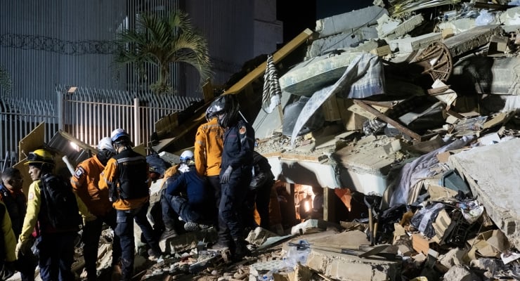 Emergency responders in helmets and orange vests search rubble after a collapsed building at a daylight disaster site
