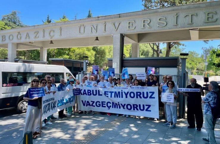 Group of protesters outside Boğaziçi University gates holding a large banner that reads 'Kabul Etmiyoruz Vazgeçmiyoruz' with smaller protest signs visible.
