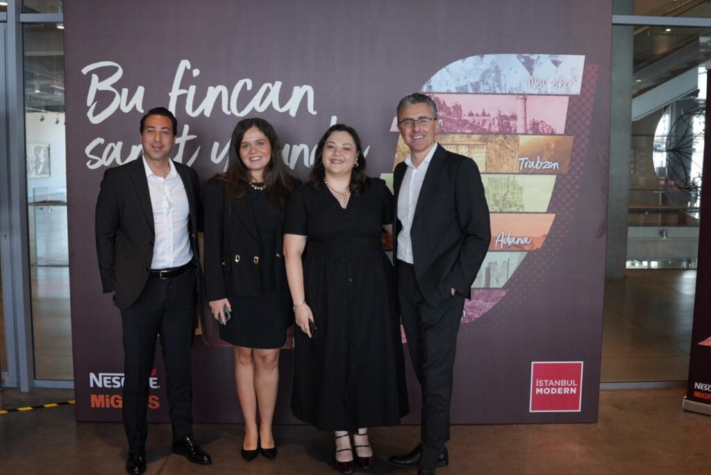 Four professionals posing in front of a purple event banner, two men and two women in formal black attire.