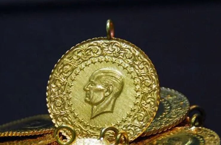 Gold coins piled together with a large engraved round pendant showing a profile, highlighting wealth or jewelry collection.
