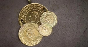 Gold antique coins with embossed portraits arranged on a dark surface, some overlapping like a pendant or charm set on a stringed loop.