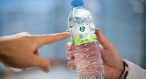Two hands exchanging a bottled water: one hand holding the bottle, the other reaching to receive it.