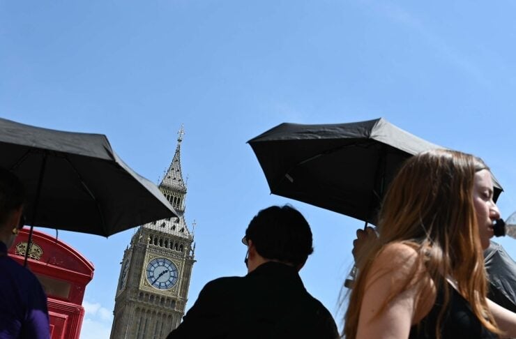 Tourists with black umbrellas on Westminster Bridge; Big Ben rises in the background, a red phone booth on the left.