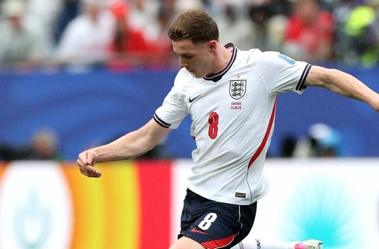 England midfielder in a white jersey with number 8 kicking a soccer ball during a match on a green field.