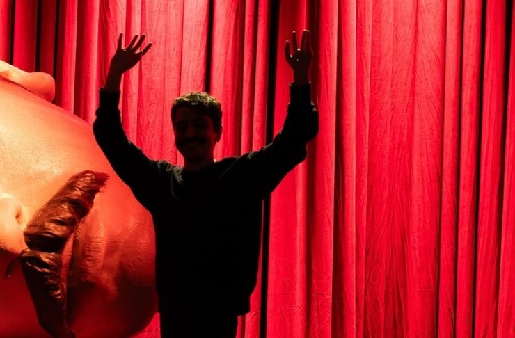 Silhouette of a person with arms raised beside a large red elephant sculpture on a stage with red curtains.