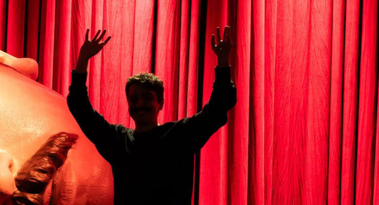 Silhouette of a person with both arms raised on a red theater curtain backdrop.