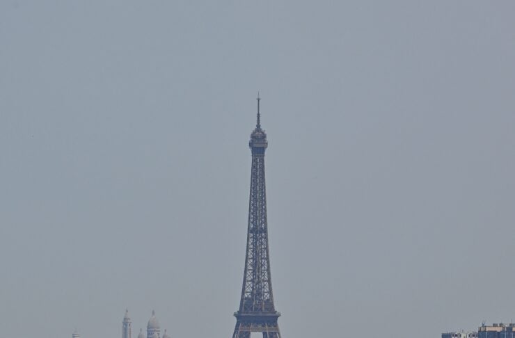 Eiffel Tower rising above Parisian rooftops on a clear day, with a dense cityscape in front. (informative)