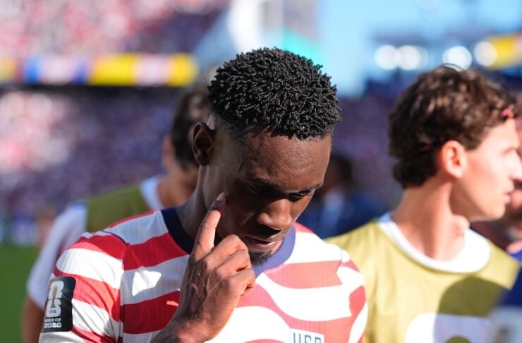 USA soccer player wearing jersey number 20 touching his temple while looking down on the field on a sunny day.