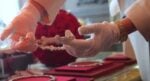 Gloved hands hold a silver bracelet with cross-shaped links in a jewelry store display case.