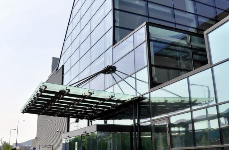 Glass-front office building with a metal-and-glass canopy over the entrance; bicycles parked outside the door.