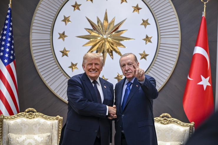 Trump and Erdogan shake hands in a formal room, Erdogan pointing toward the camera, with American and Turkish flags behind them.