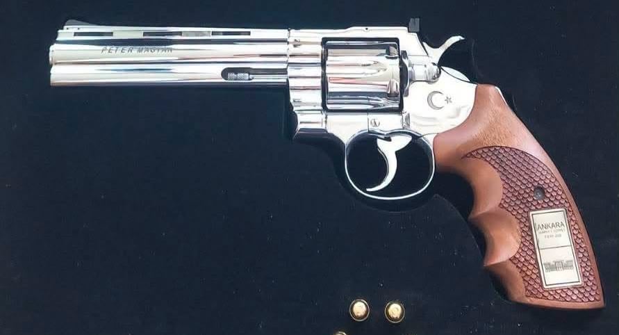 Polished silver revolver with a brown textured grip on a dark surface, with two bullets nearby.