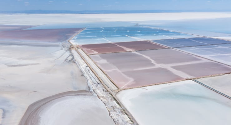 Aerial view of salt evaporation ponds with colorful rectangular basins in blue, pink, and brown, separated by narrow dikes.