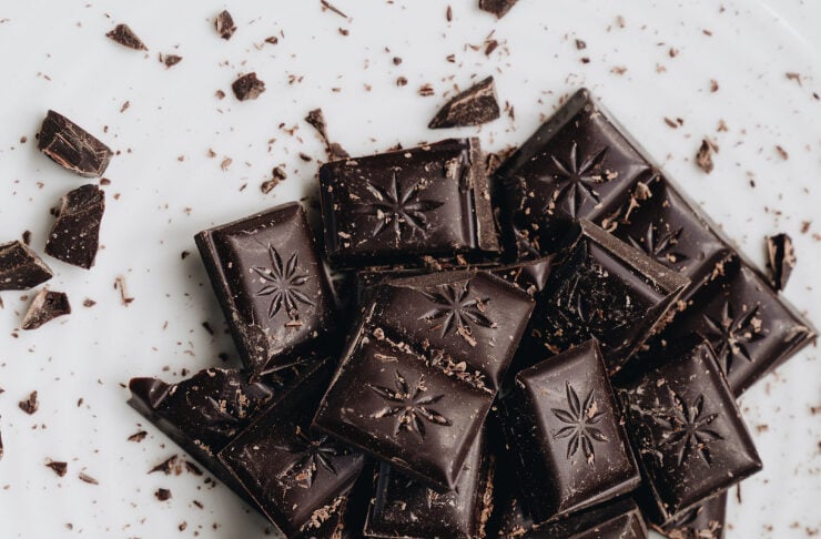Dark chocolate pieces with a star-shaped pattern, broken into shards on a white plate with cocoa crumbs nearby