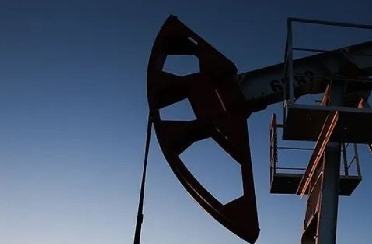 Silhouette of an oil pump jack against a sunset sky on the horizon.