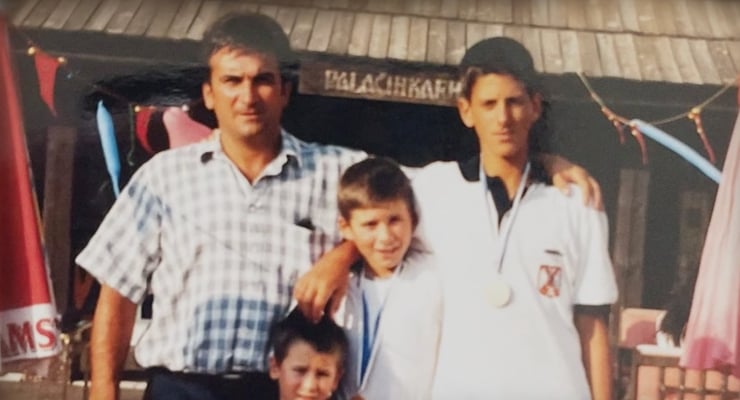 Family of four posing together outdoors; two children wear medals around their necks.