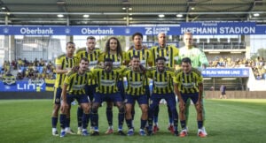 Ten soccer players in yellow-and-blue striped uniforms pose for a group photo on the field, with a goalkeeper in green; stadium banners and stands in the background.