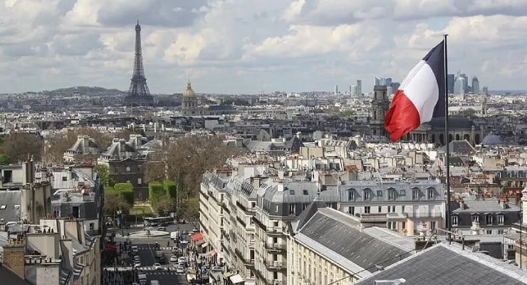 Panoramic view of Paris rooftops with the Eiffel Tower in the distance and a French flag in the foreground.