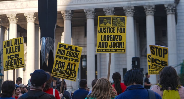 Protesters hold bright yellow signs with messages like 'Jail all killer ICE agents' and 'Justice for Lorenzo and Joan' outside a columned government building.