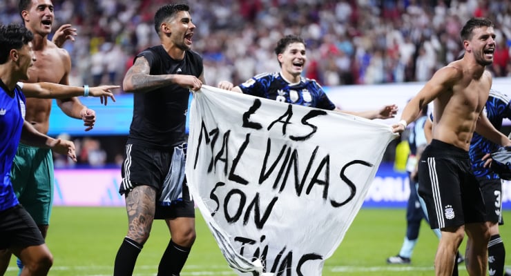 Soccer players celebrate on the field, holding a white banner that reads 'Las Malvinas son nuestras'.