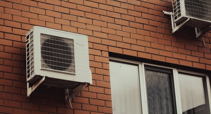 Outdoor wall with two window AC units mounted on a brick facade near a window with blinds