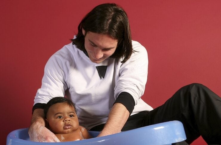 Caregiver washing a baby in a blue plastic tub, with a rubber duck nearby on a red background.