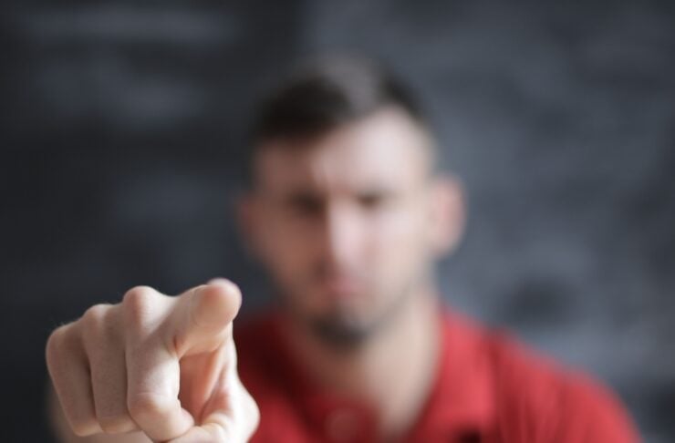 Person in a red polo points directly at the viewer with a focused, blurred background behind them.