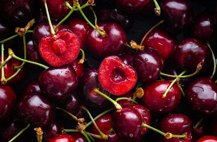 Pile of ripe red cherries with green stems, a few halved to reveal bright red flesh.