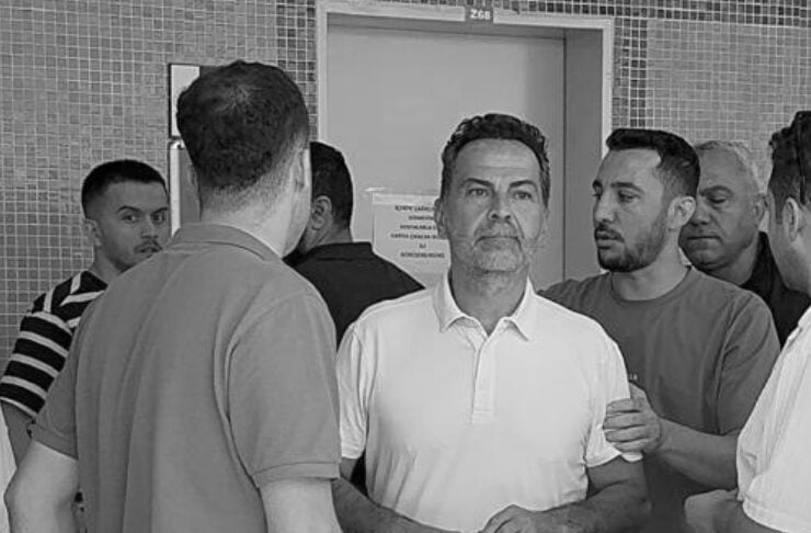 Group of men standing in a doorway area, one man in a white polo holds a water bottle while others stand nearby.