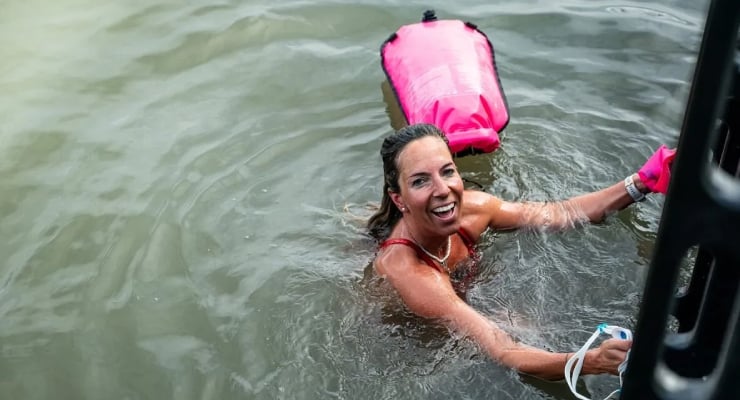 Woman in water happy, wearing a pink life jacket, reaching toward a boat.
