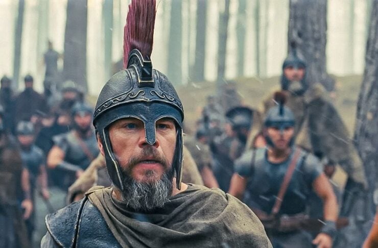 A bearded man in a Roman-style helmet leads a group of soldiers in a misty forest.