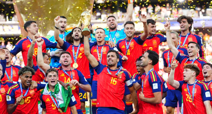 Spain national football team players celebrate winning the trophy on the field, confetti falling around them with medals visible.