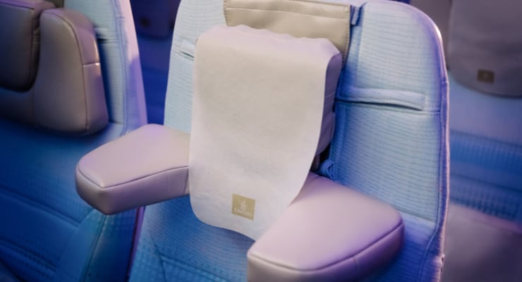 Blue airline seat with a white towel draped over the headrest in a cabin.