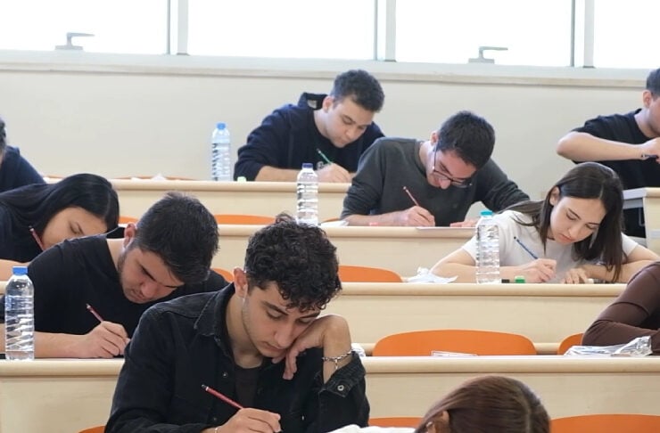 College students in a classroom taking an exam, focused on their papers with pens in hand and water bottles on desks