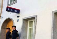 Two uniformed police officers standing guard outside a German police station, near an arched doorway and a window.