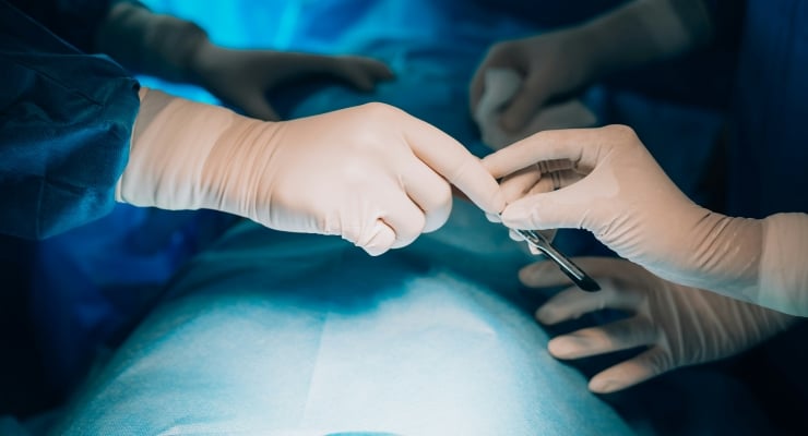 Surgical team in sterile gloves exchanging forceps over a patient on the operating table.