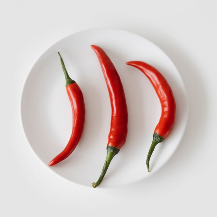Three red chili peppers arranged on a white plate for cooking or display