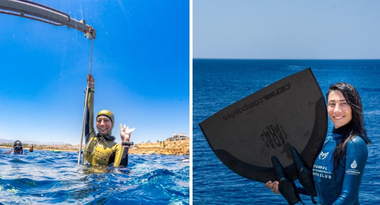 Diver in a yellow wetsuit raises a line above the ocean surface, another diver visible in the water behind near a coastal town.
